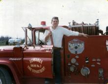 An image of a Cosmo Boyd in his 20s standing in the door of a fire truck